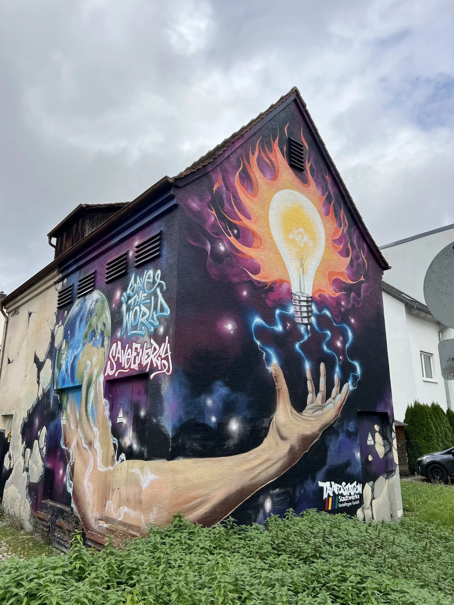 Großes Street-Art-Mural mit einer Hand, die eine leuchtende Glühbirne mit Flammen hält, gemalt auf eine Gebäudewand